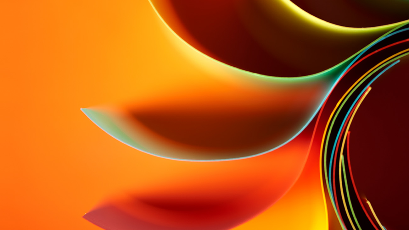 Abstract digital artwork featuring curved, layered shapes in vibrant orange, yellow, green, and red tones, creating a dynamic and visually striking composition against an orange background.