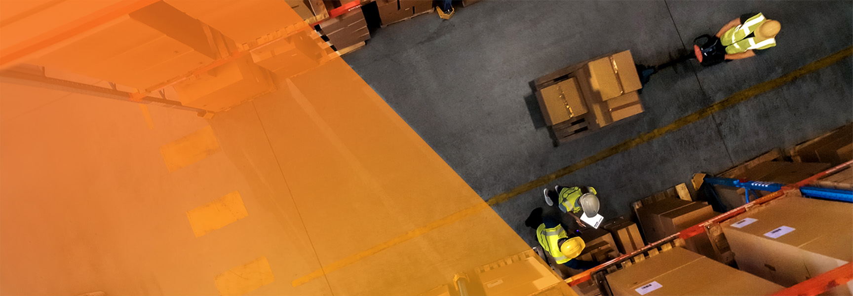 Top view of two warehouse workers wearing safety vests and helmets, moving boxes in an industrial setting. Brown boxes are stacked around them, with an orange translucent overlay on the left side of the image.