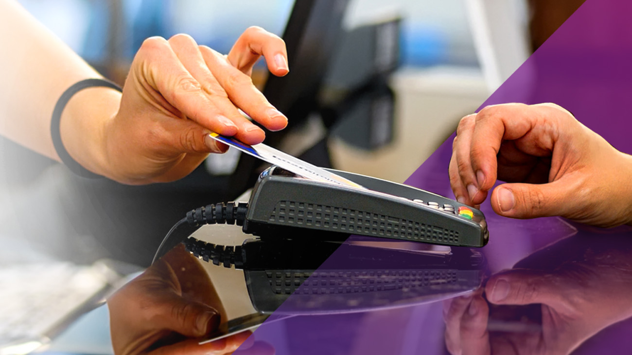 A hand swiping a credit card through a card reader on a counter. A second hand is visible, possibly about to interact with the card reader. The background is a blend of white and purple.