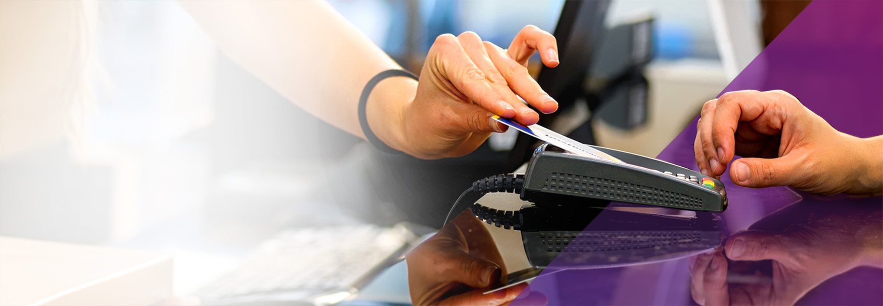 A person is swiping a credit card through a payment terminal on a glossy surface. Another hand is visible, poised to receive the card. The background is blurred with a mix of white and purple areas.