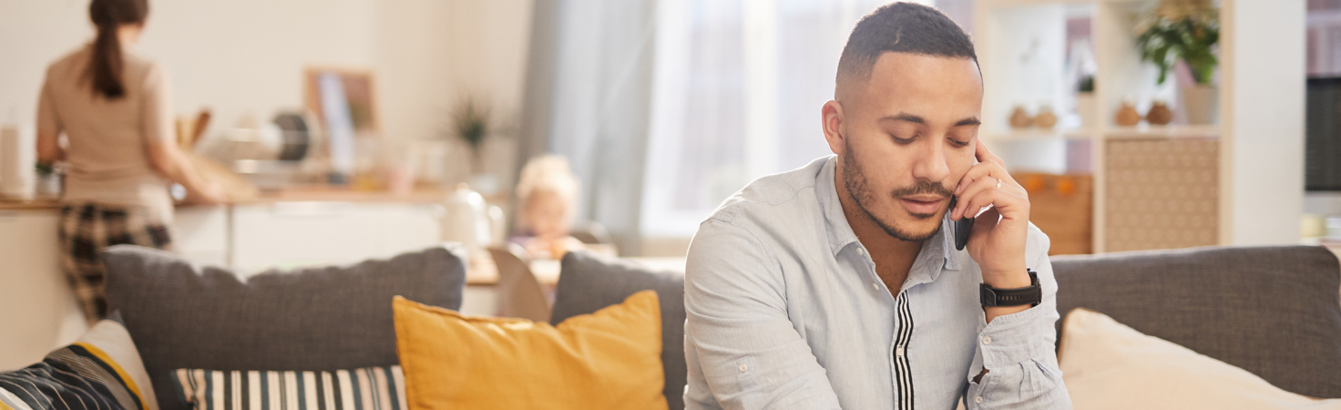 man on the phone working from who while wife stands in the kitchen