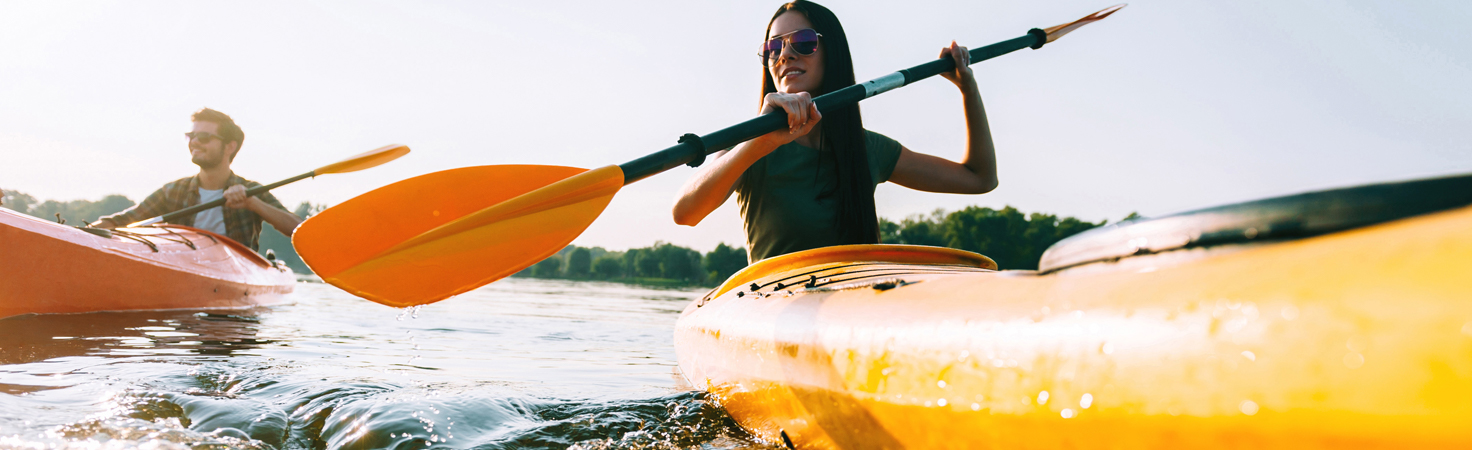 Two people kayaking on a calm lake explore the essence of hedonic rewards. The person in the foreground paddles a yellow kayak, sporting sunglasses, while savoring the suns warmth. Behind them, a companion in an orange kayak shares this blissful escape amidst trees and tranquility.