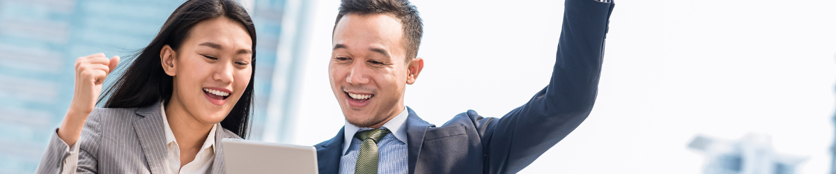 Two business professionals, a man and a woman, celebrate while looking at a tablet. Dressed in formal attire against the blurred cityscape, their smiles reflect the spirit of employee appreciation quotes as they achieve success together.