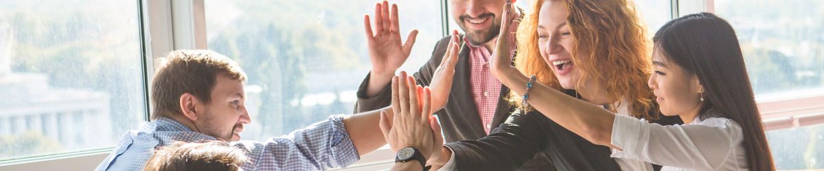 Five people are gathered near a window, smiling and giving high-fives to each other. Bright natural light fills the space, creating a positive and energetic atmosphere reminiscent of employee appreciation quotes. They appear to be celebrating or sharing a successful moment.